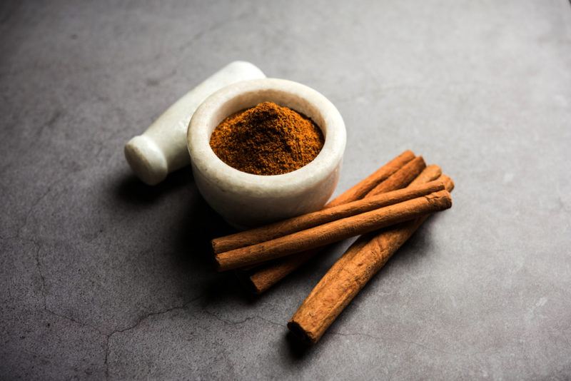 A morter containing cinnamon powder, a pestle, and cinnamon sticks