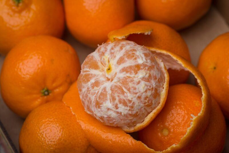 a closeup image of a pile of clementine with one on top that is partially peeled