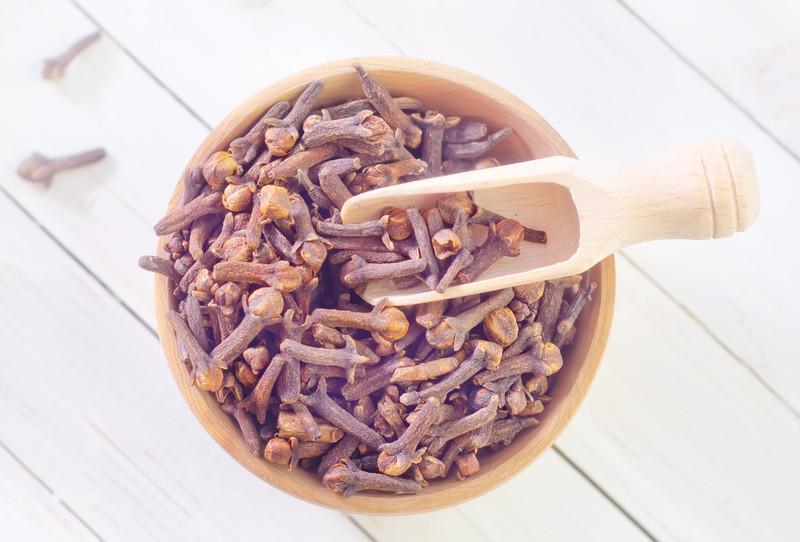 top view image of a wooden bowl full of cloves with wooden scoop on a wooden table