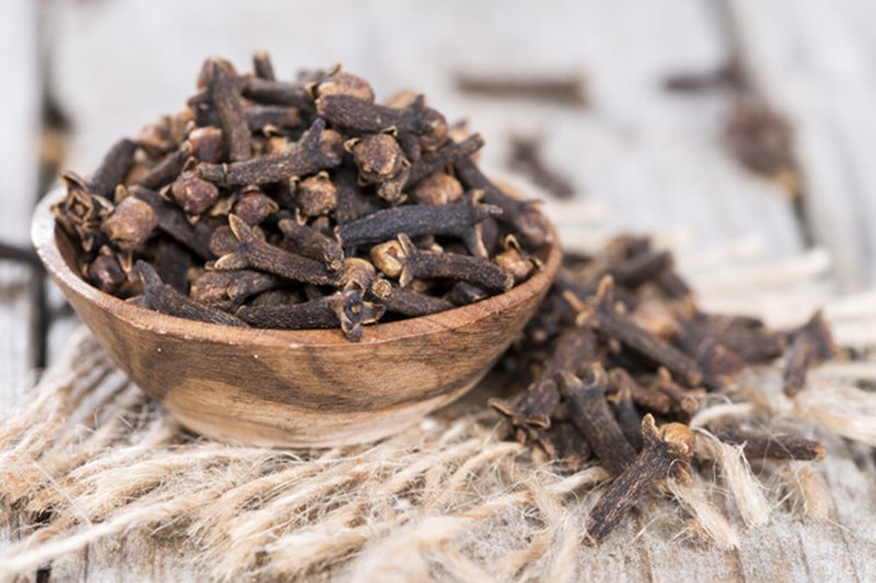 a wooden bowl full of cloves resting on a piece of cloth sack with lose cloves around it