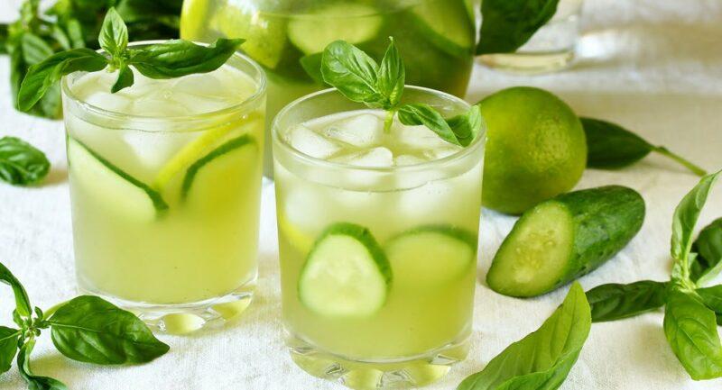 Two glasses of cucumber juice with ice, with cucumbers alongside of it