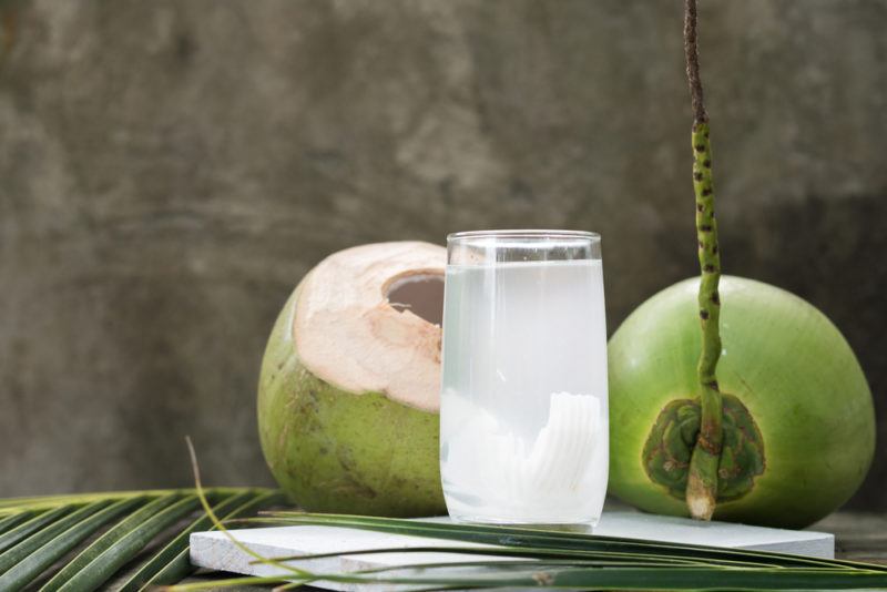 A glass with coconut water and two green coconuts on a table