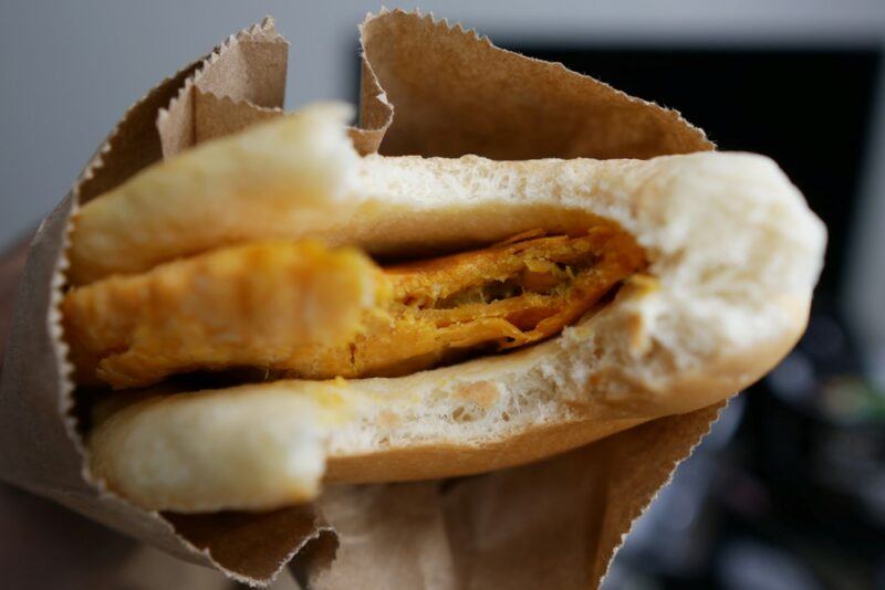 A piece of coco bread in a paper bag that's been folded over around some type of meat filling