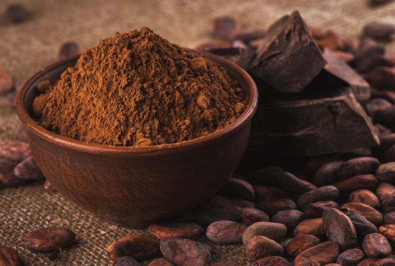 A bowl of cocoa powder, some dark chocolate and some cocoa beans