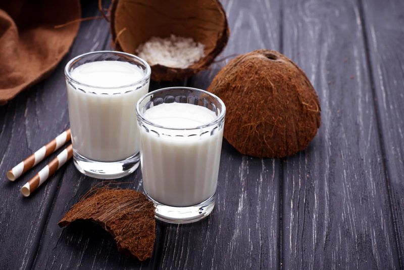 Two glasses of coconut milk next to coconut shells