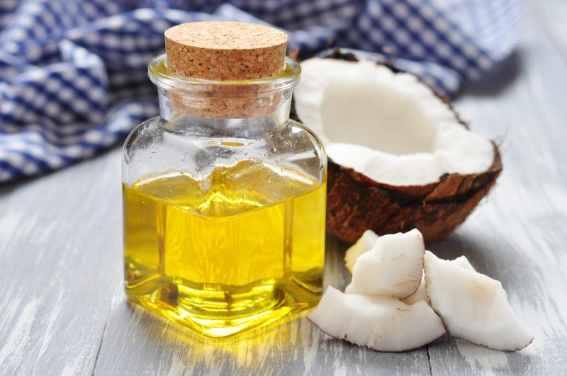 A small jar of coconut oil on a table next to half a coconut and coconut chunks