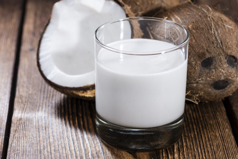 A whole coconut and a coconut half, next to a glass of coconut milk