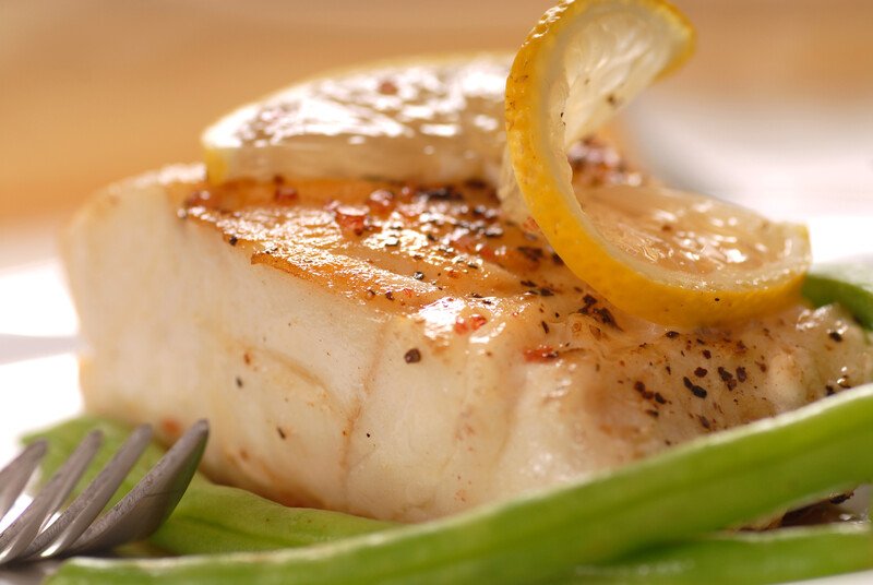 This photo shows a close-up of cooked cod with a lemon slice on top.