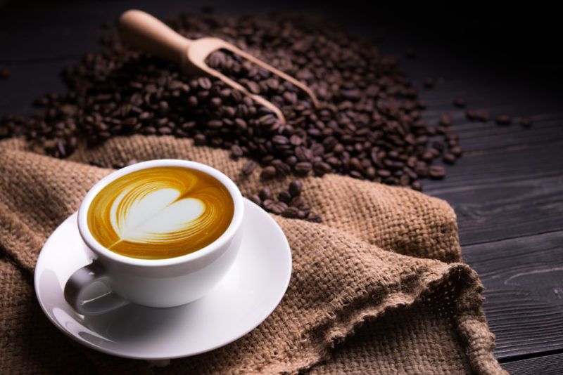 A mug of hot coffeee and a scoop of coffee beans