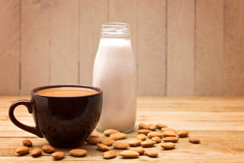 A bottle of almond milk with an almond milk coffee next to it