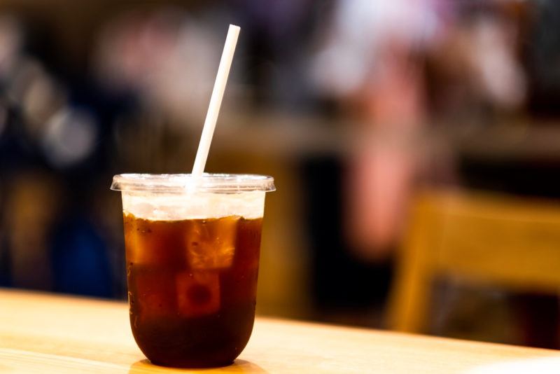 A plastic container of iced coffee with soda water and a straw