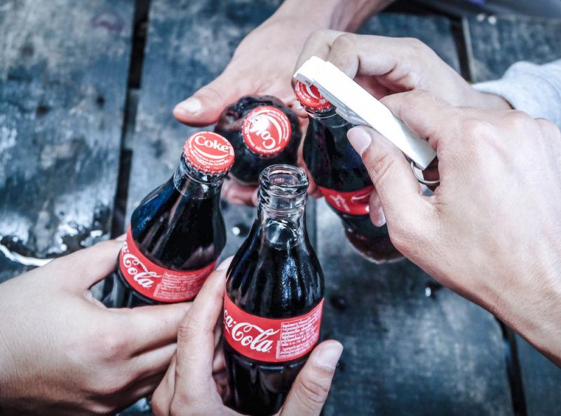 Hands holding cola bottles opening them