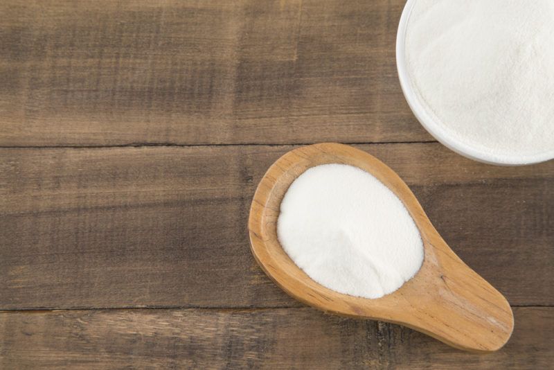 A spoon and a white bowl filled with collagen powder