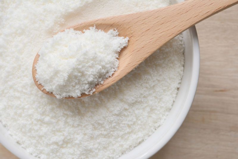 A white bowl with collagen powder and a wooden spoon with more