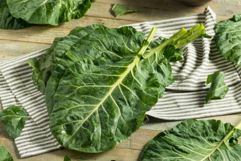 Various raw collard leaves on paper and a wooden table