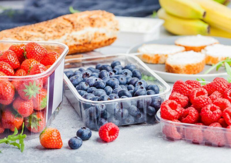 A picnic with bread and three containers of fruit, including raspberries, strawberries, and blueberries