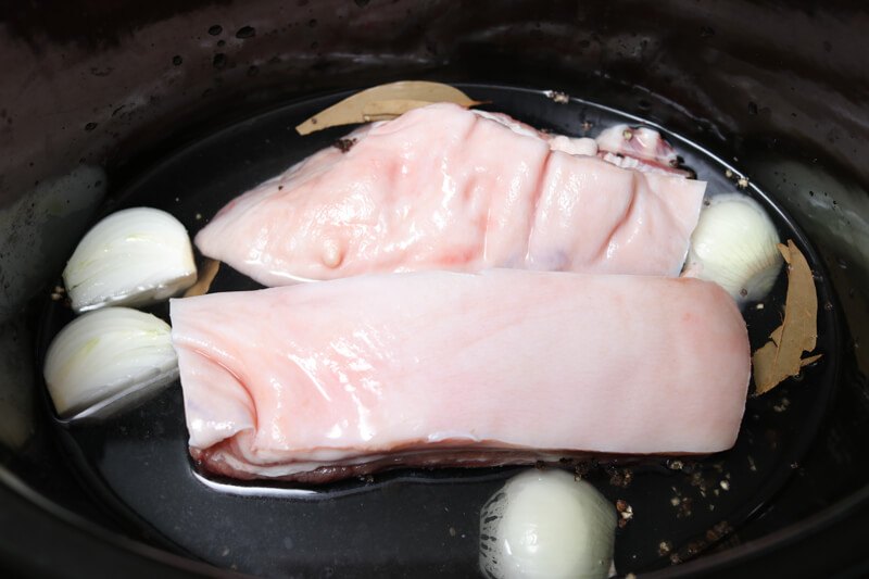 Pieces of uncooked pork belly in a slow cooker with onions and spices