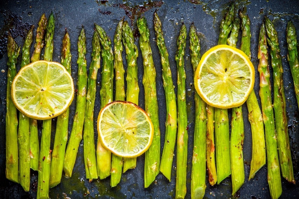 A cooking tray with baked asparagus and lemon slices