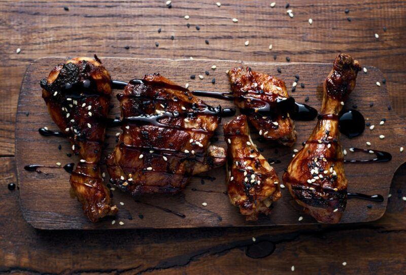 A wooden board with cooked pieces of chicken that have balsamic vinegar sprinkled on top