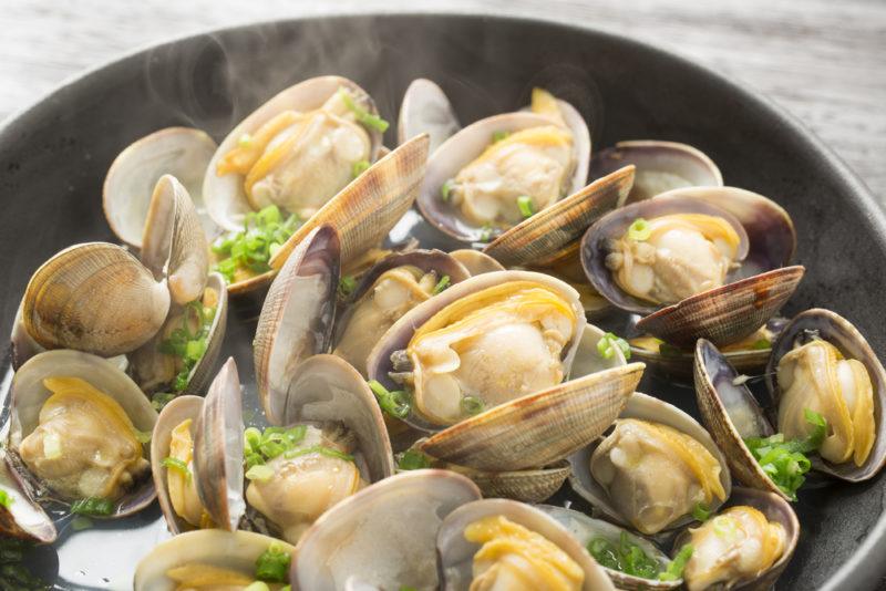 A black frypan that contains cooked clams that are still steaming