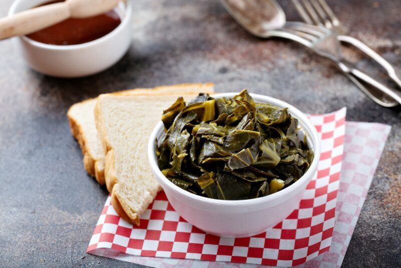 A table at a restaurant with cooked collard greens and bread on a napkin, next to a couple of forks and a small dish of sauce