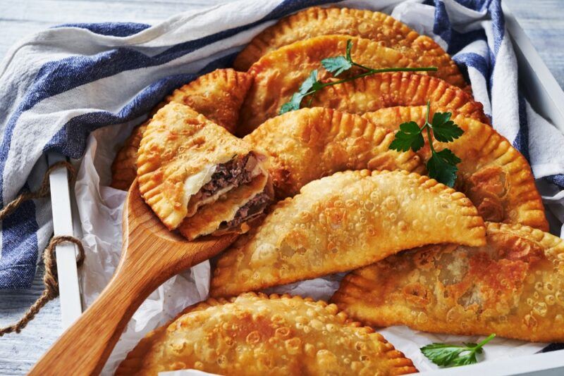 A collection of fried empanadas. One is on a spoon, has been cut open and is filled with meat