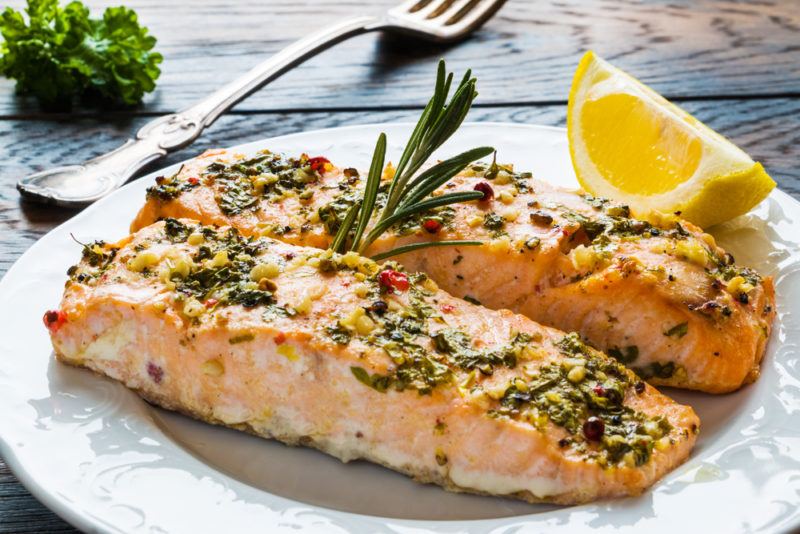 Two pieces of cooked salmon on a plate with rosemary and a fork