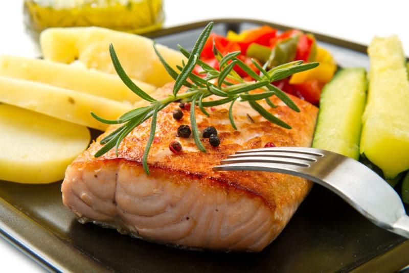 A piece of cooked fish on a black plate next to potatoes and a fork