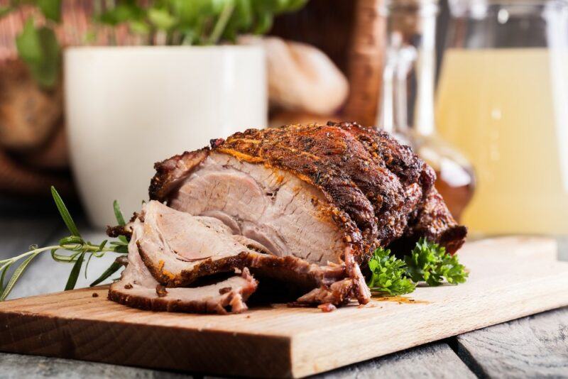 A wooden board with a cooked piece of pork that's been sliced