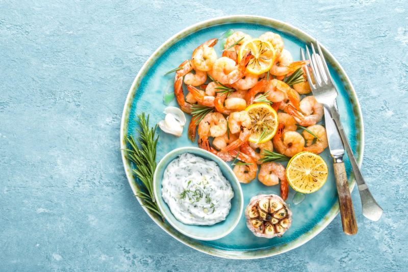 A blue plate with cooked shrimp and dip