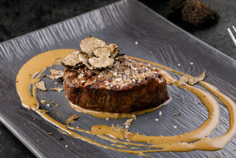 A black plate with a cooked steak and sliced truffles