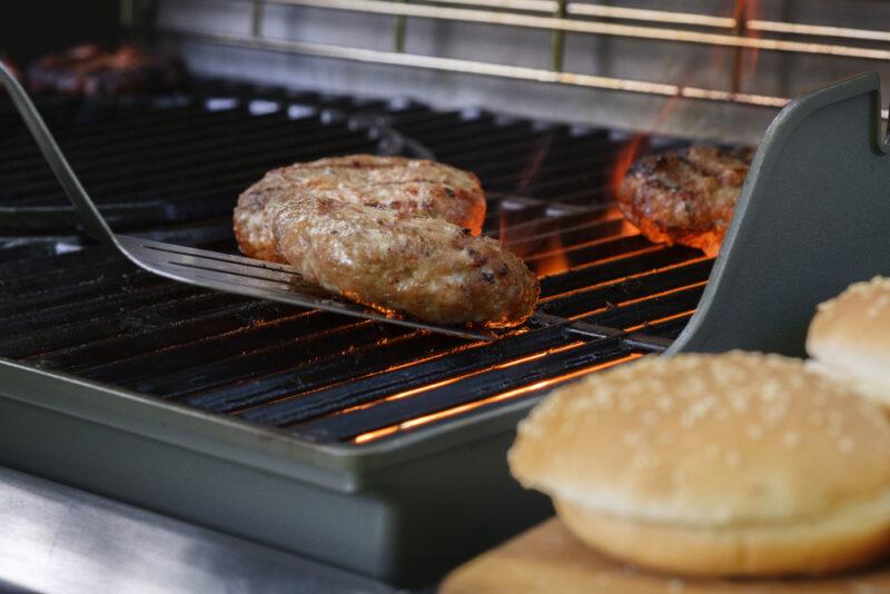 Cooking burgers on an outdoor grill alongside burger buns