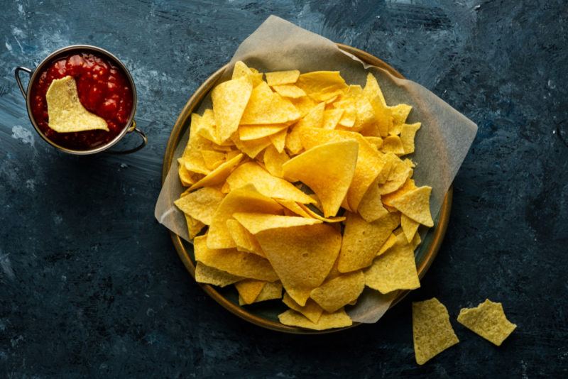 A dish containin fresh corn chips, next to a small bowl of salsa