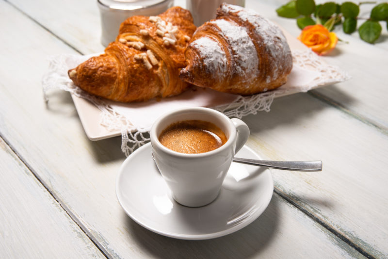 A white plate with two cornetto pastries behind a mug of coffee