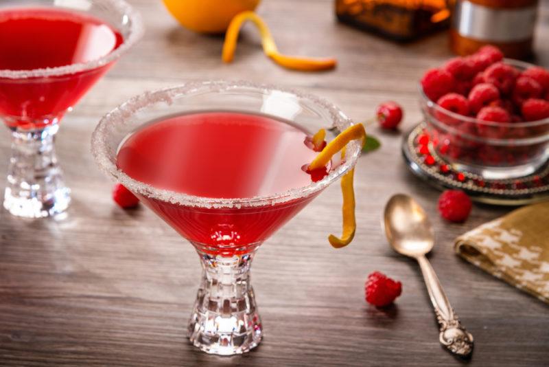 Two cosmopolitan cocktails in cocktail glasses with berries and other garnishes on a table