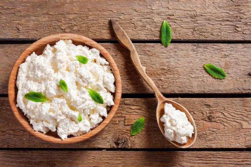 Top down image of a wooden bowl and wooden spoon containing cottage cheese