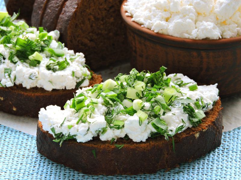 Toast with cottage cheese and greens, with a bowl of cottage cheese in the background