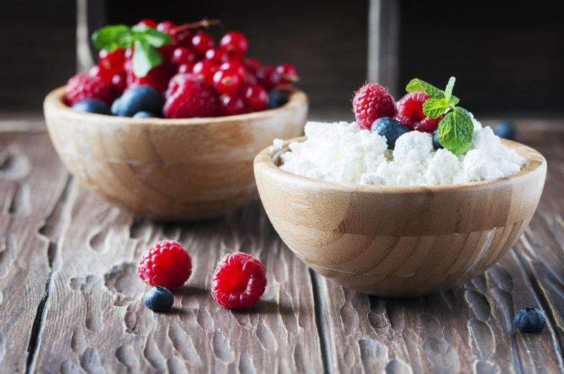 A wooden bowl of cottage cheese with another bowl of berries