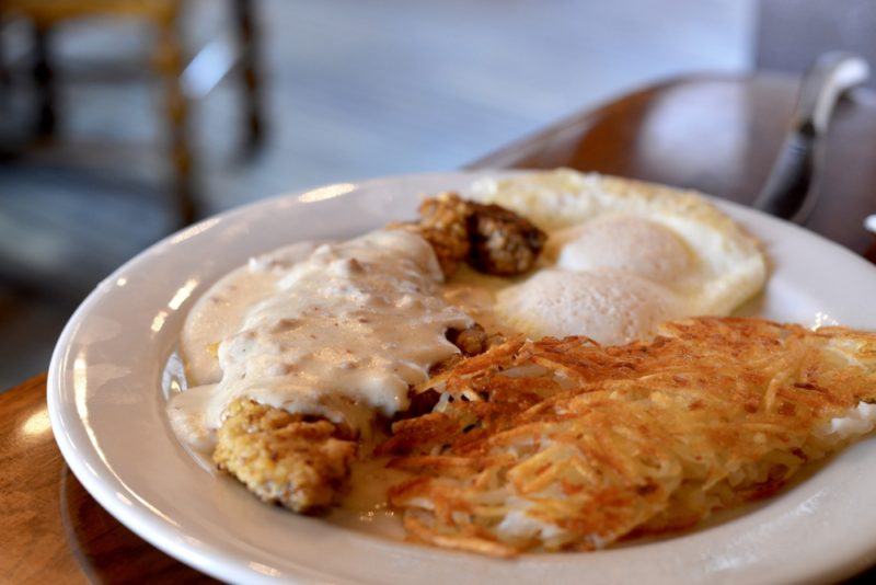 A Southern breakfast that includes country fried steak and eggs on a white plate