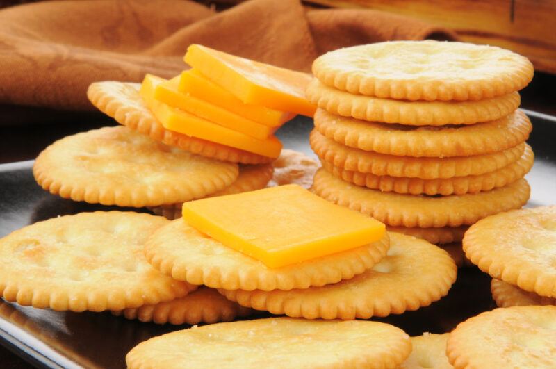 Stacks of round crackers and square slices of cheese rest on a dark surface near a brown cloth.