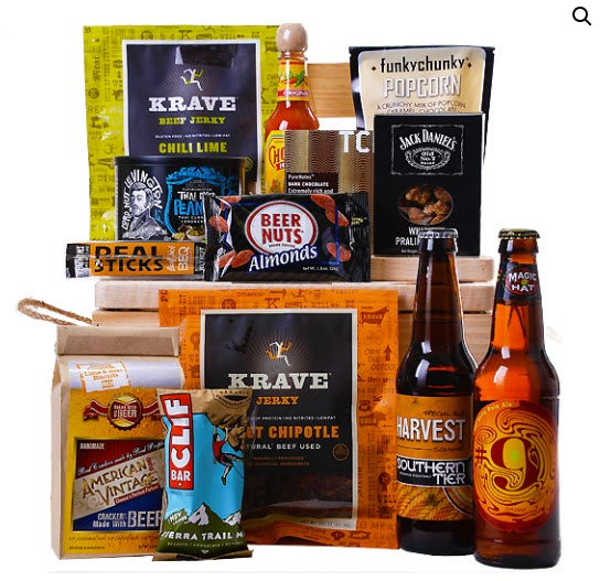 A wide selection of snacks resting on top of a crate, with more in front of it, along with 2 bottles of beer. 