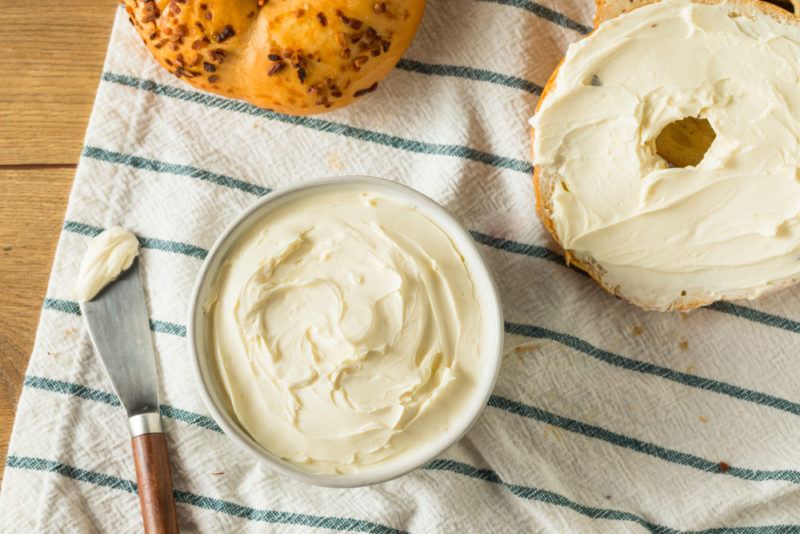 Cream cheese on a bagel and in a white bowl on a cloth