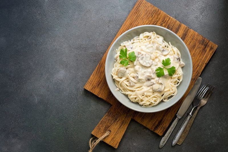 A gray plate with a creamy mushroom pasta dish on a wooden board