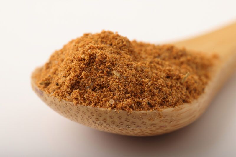 a closeup image of a wooden spoon full of Creole seasoning resting on a beige-colored surface