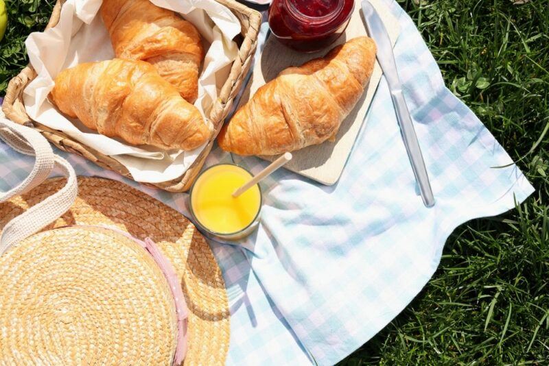 A blue and white picnic blanket with croissants, jam, and orange juice