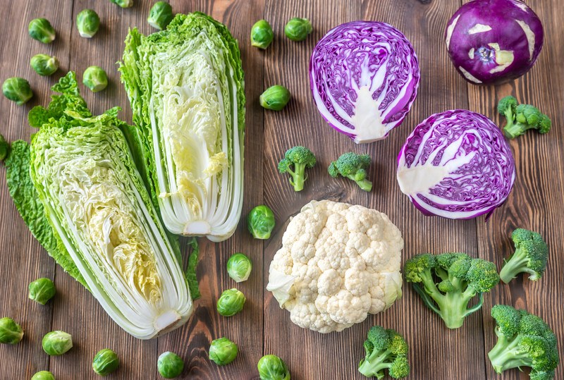 This photo shows several types of cabbage, brussels sprouts, broccoli, and cauliflower on a wooden table.