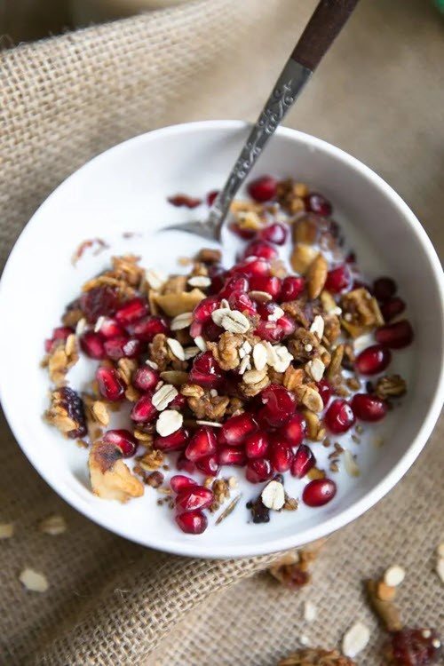 A large white bowl containing crunchy fall spice granola with pomegranate arils