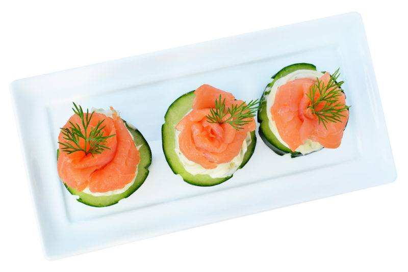 A white plate with appetizers of cucumber, salmon, and cream cheese