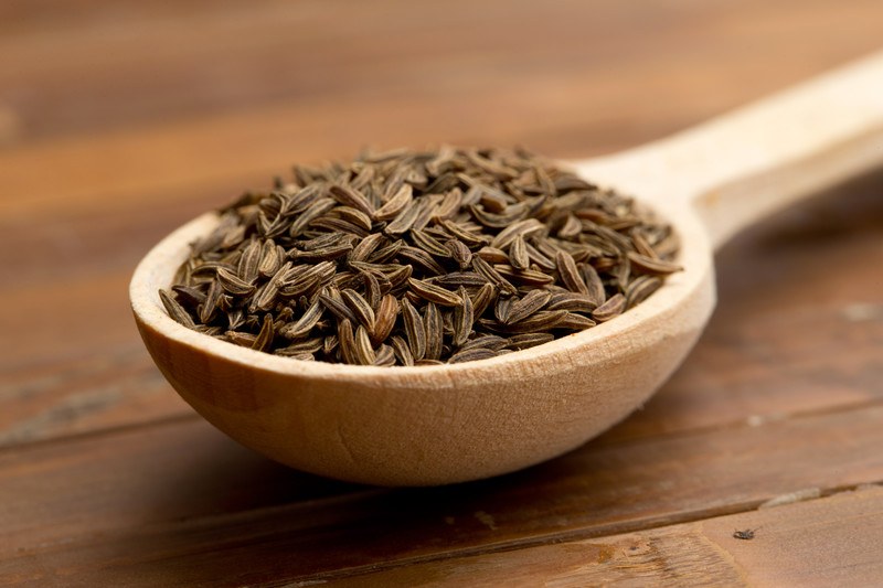 closeup image of a wooden ladle full of cumin seeds on a wooden surface