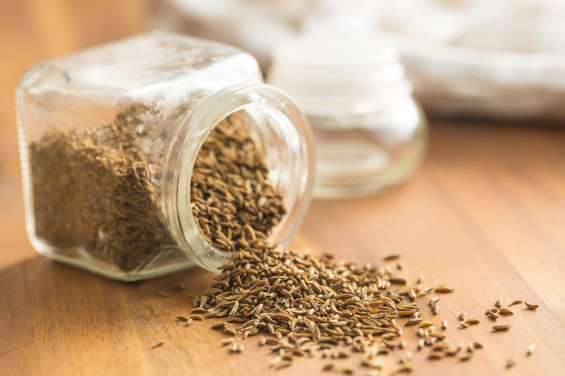 cumin pouring out of a small toppled over spice jar on a wooden surface